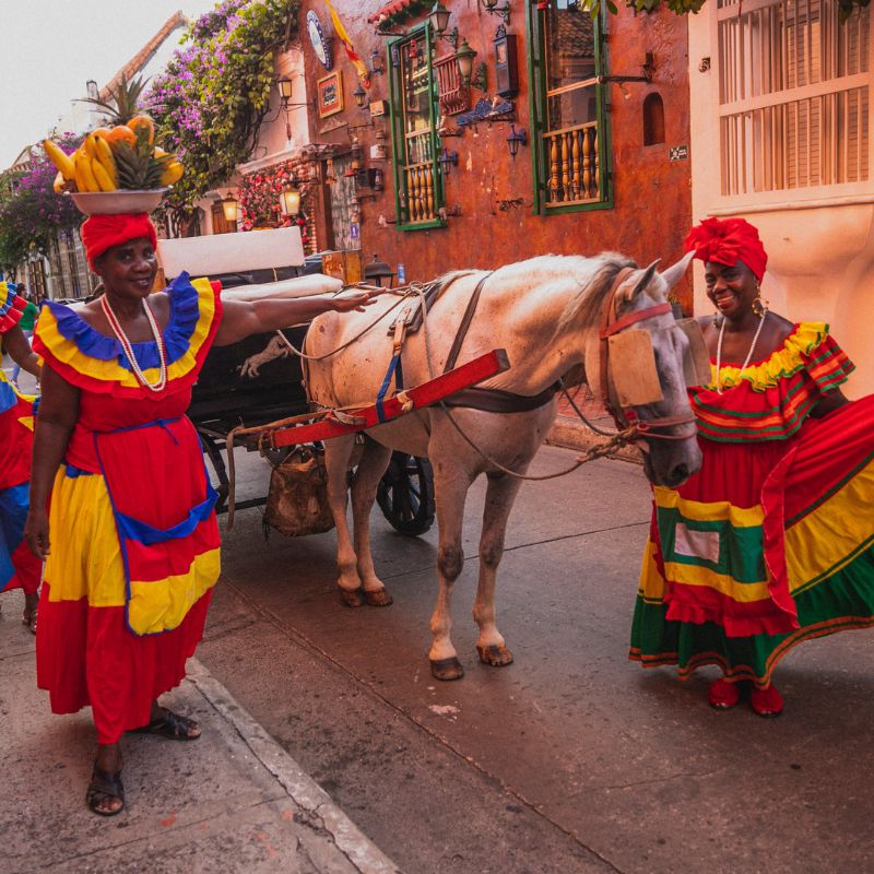 Women colourfully dressed in Cartagena showcasing goods and leading a horse down the road.