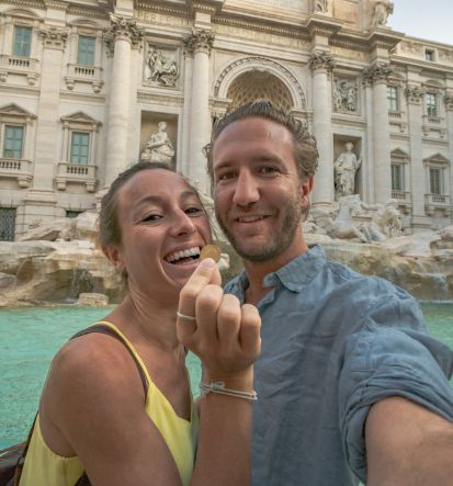 A couple holding a coin to through in the Trevi statue