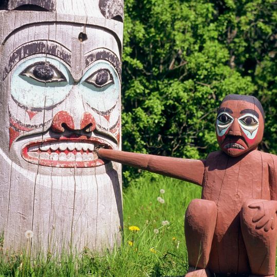Totem pole putting its hand in the other totem pol's mouth in Ketchikan